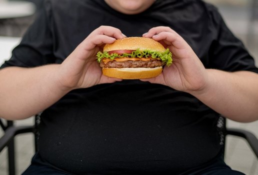 A photo of a young obese person holding a hamburge K6 MV Yhce Qg On GSB Hsfm Sw Q is L Zqc GS Qf2tf7 Sqz UEP Ew