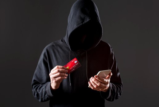 Vista frontal do hacker masculino segurando o smartphone e cartao de credito