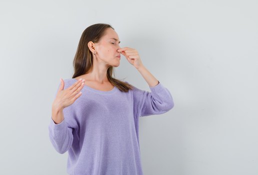 Senhora jovem beliscando o nariz devido ao mau cheiro em uma camisa casual e parecendo enojada vista frontal