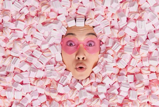 Surpresa jovem asiatica usa oculos escuros em forma de coracao e parece maravilhada afogada em um marshmallow macio rosa chocada com quantas calorias ela consumiu indo para fazer um fofo saboroso