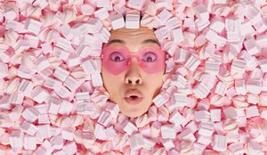 Surpresa jovem asiatica usa oculos escuros em forma de coracao e parece maravilhada afogada em um marshmallow macio rosa chocada com quantas calorias ela consumiu indo para fazer um fofo saboroso